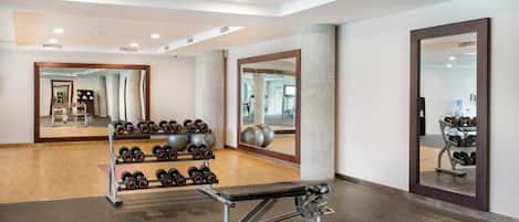 Un gimnasio con equipo de ejercicio, una banca y un espejo.