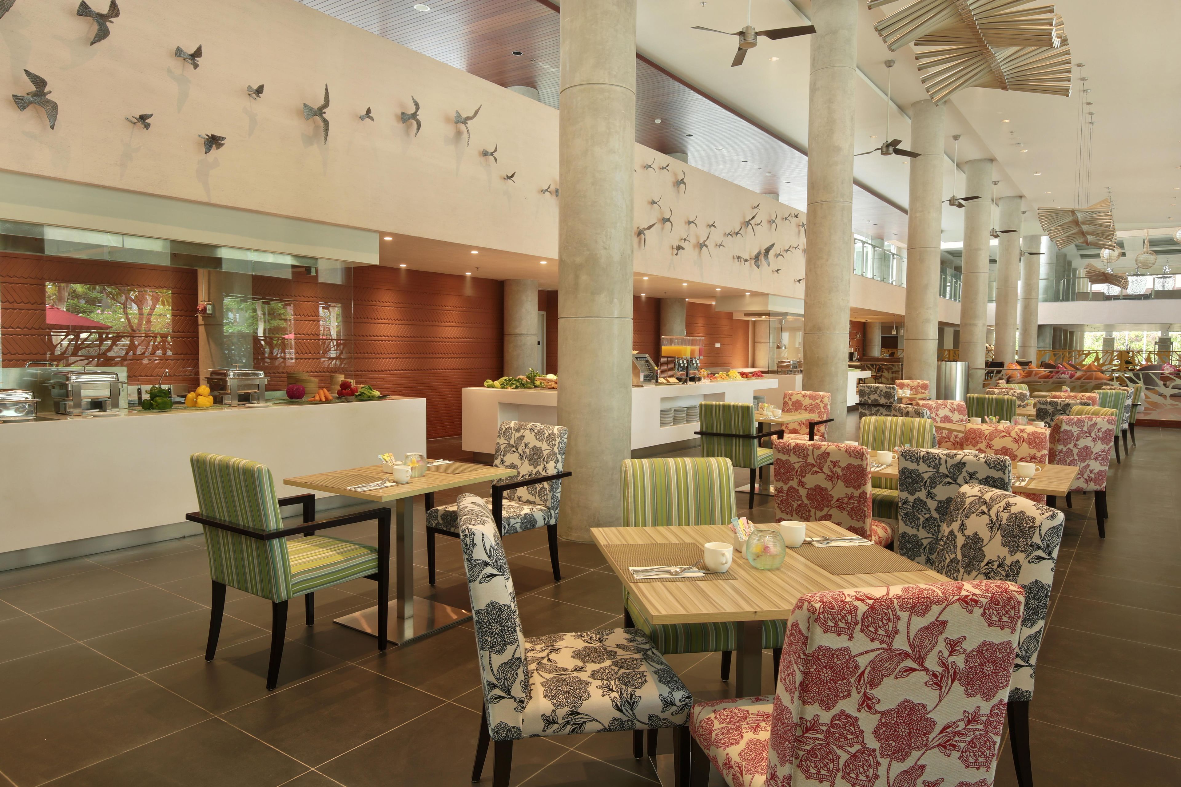 Amplia zona de comedor de hotel con varias mesas y sillas, un mostrador de buffet y decoración mural.