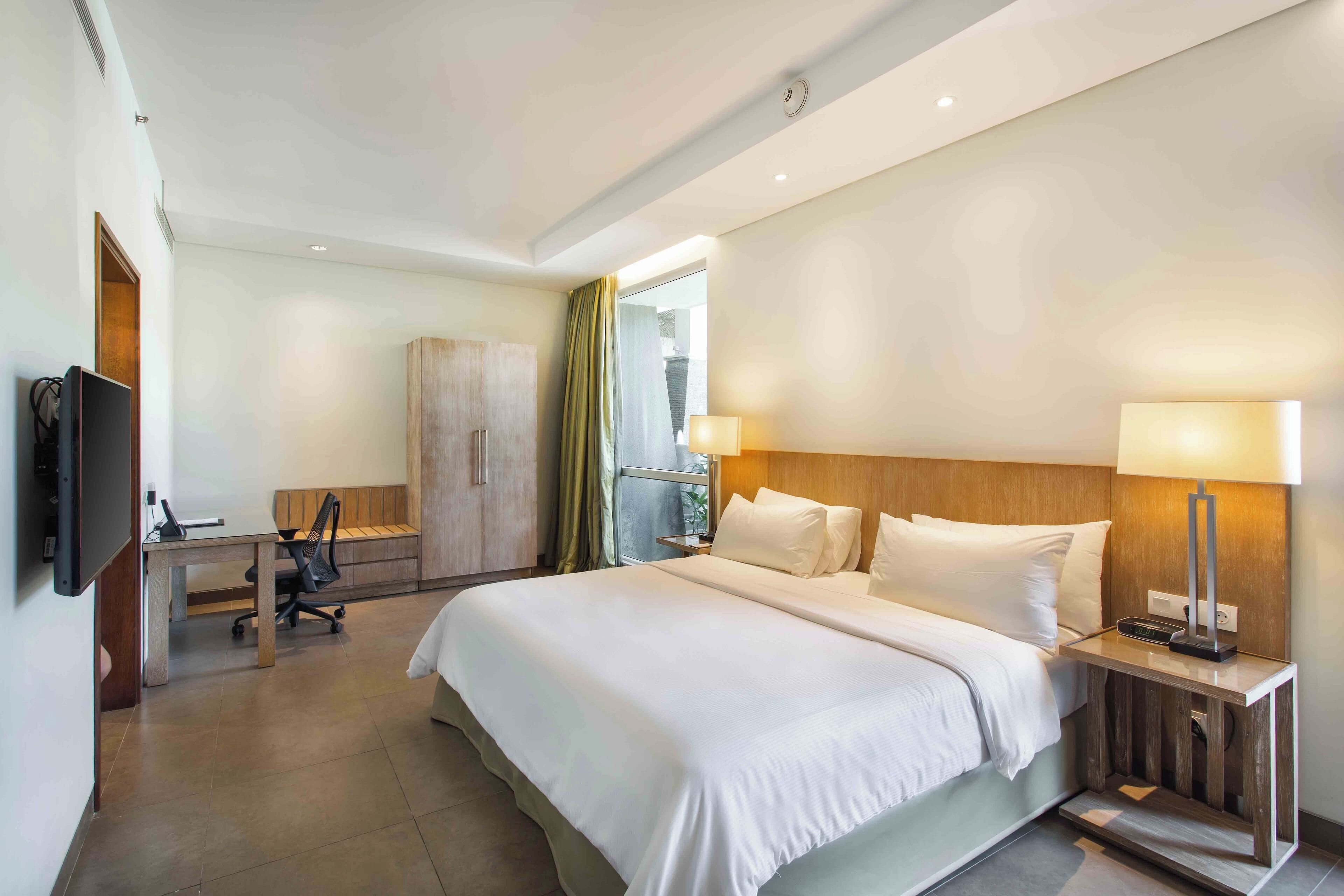 Une chambre d’hôtel avec un grand lit, des tables de chevet, un bureau, une chaise et un téléviseur.