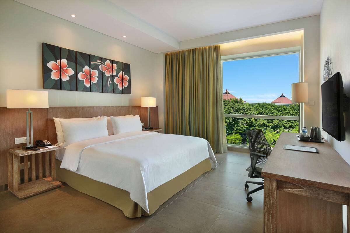 Une chambre d’hôtel avec un grand lit, un bureau avec une chaise, une télévision et une fenêtre avec des rideaux.