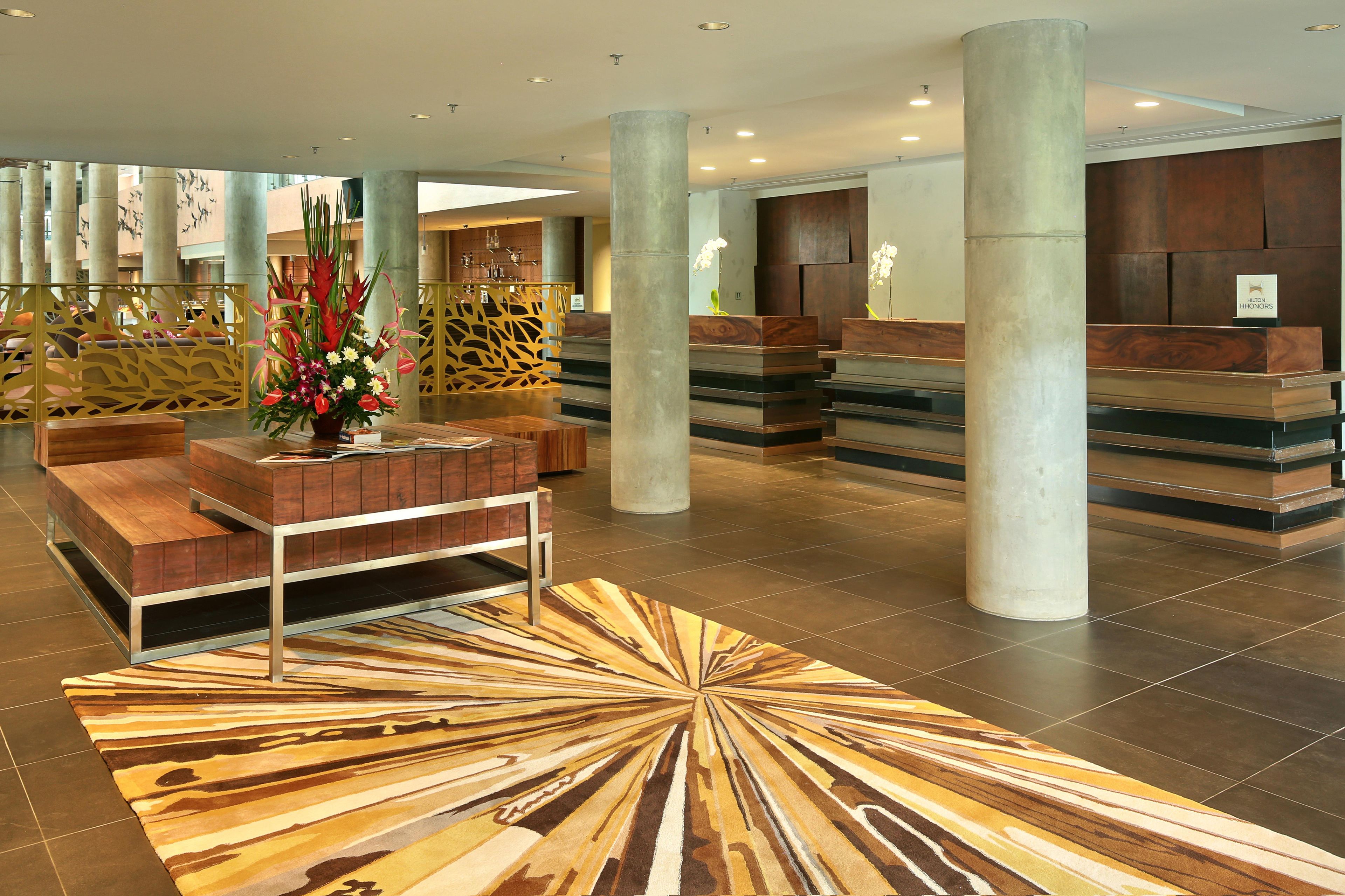 A hotel lobby with a reception desk, seating area, and decorative plants.