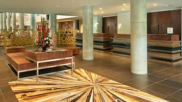 A hotel lobby with a reception desk, seating area, and decorative plants.