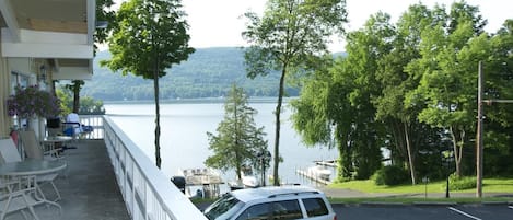A view from a balcony overlooking a lake with boats docked, surrounded by trees and a parking area with a car.