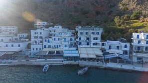 A coastal village with white buildings, a marina with boats, and a hillside in the background. - Kyma (Sfakia)