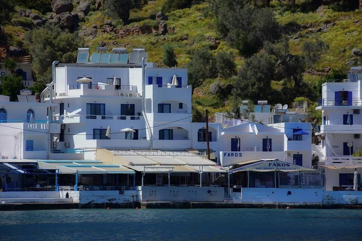 A coastal building with multiple stories, a sign for 'Faros Market', and a boat docked in front.