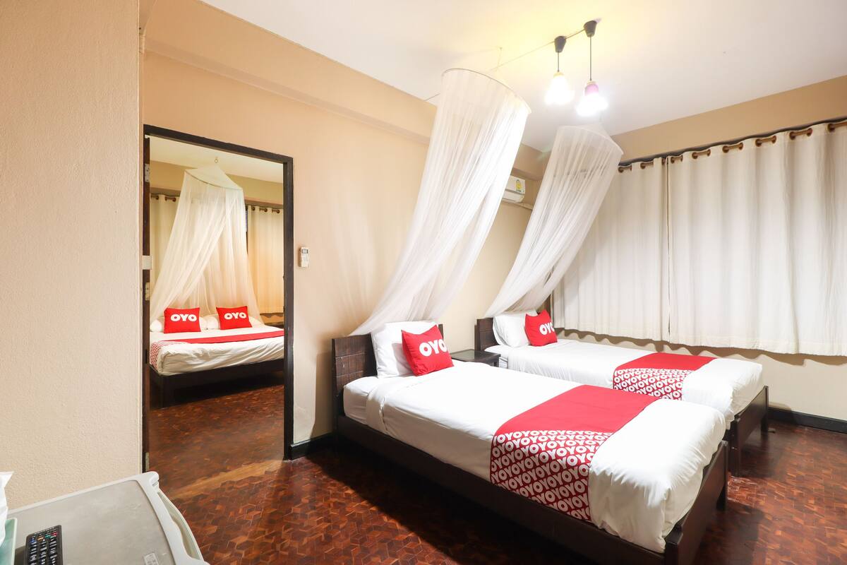 Een hotelkamer met twee bedden, elk voorzien van een hemelbedbaldakken en kussens met 'OYO'-branding.