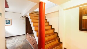 A staircase with wooden steps and a red column, leading to a landing with a door and a framed picture on the wall. - OYO 369 Micasa Guesthouse (Chiang Mai)