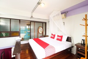 Ein Hotelzimmer mit Bett, einer Bank, einem Nachttisch, einem Holzstuhl und einem Moskitonetz.