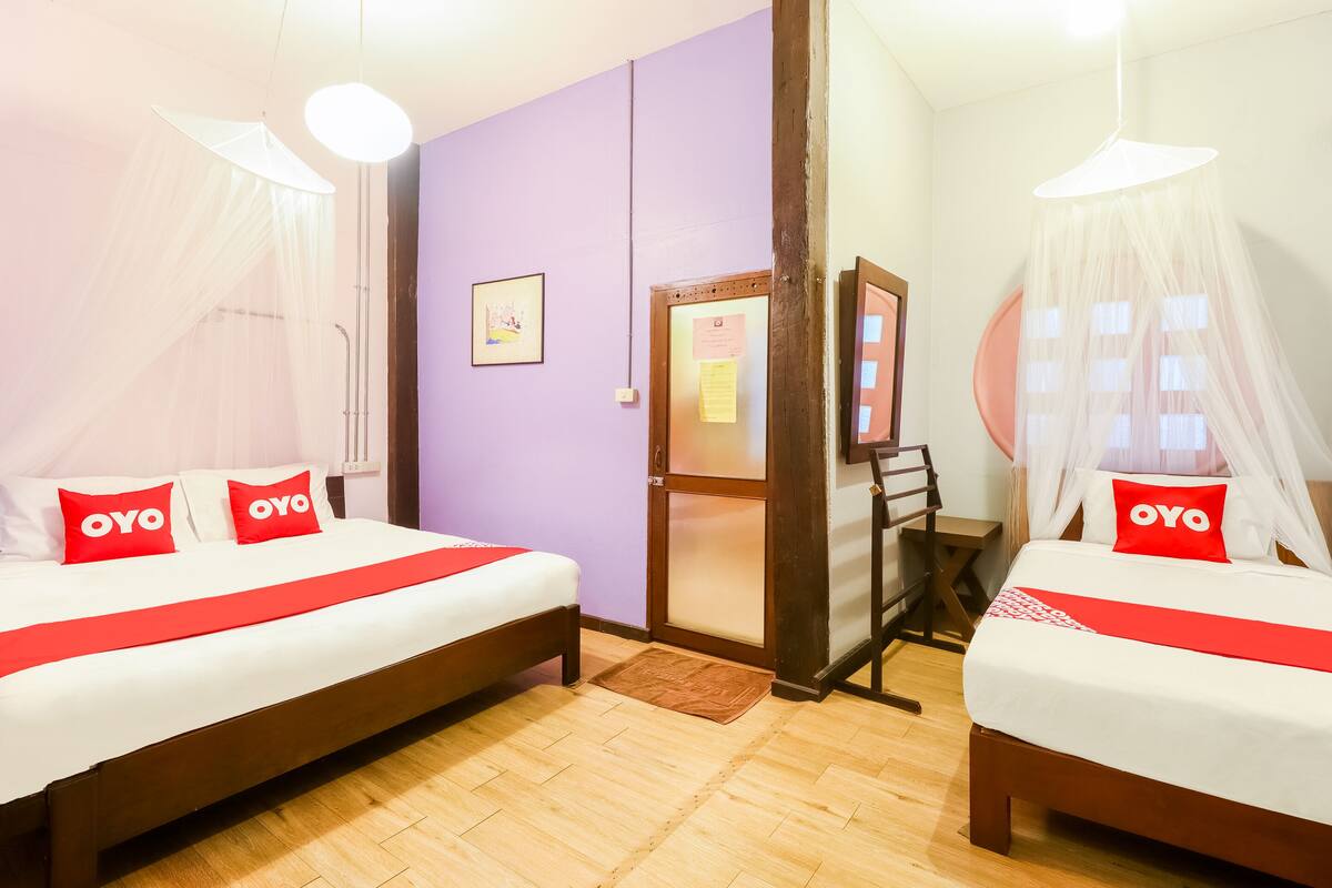 Een hotelkamer met twee bedden, elk voorzien van een hemelbed en een rood 'OYO'-kussen.