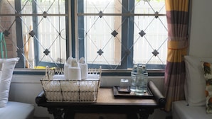A room with a window featuring a metal grid design, a wicker basket with towels, a tray with bottles, and a bed with a pineapple pillow. - Stay With Me Guesthouse (Chiang Mai)