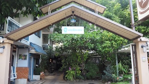 A hotel entrance with a 'Welcome' sign, a covered walkway, and lush greenery. - Stay With Me Guesthouse (Chiang Mai)