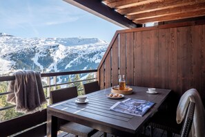 A wooden table with a view of snow-covered mountains, a glass of beer, and a newspaper. - Résidence Pierre et Vacances Premium Flaine Les Terrasses d'Hélios (Araches-la-Frasse)