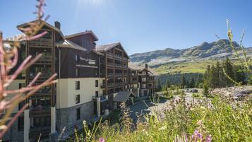 A multi-story lodge with a stone facade, multiple balconies, and a view of the surrounding mountains.