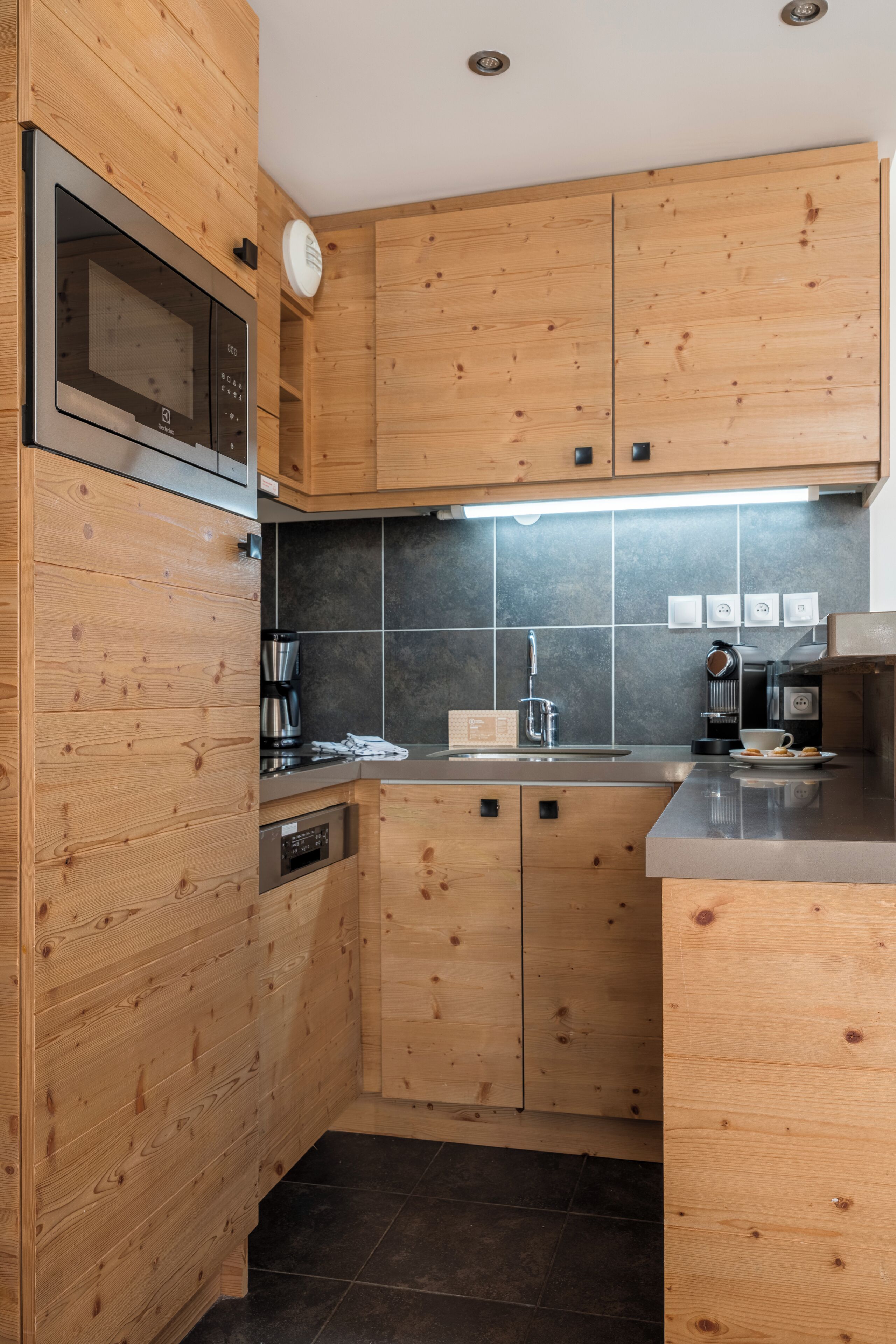 Een moderne keuken met houten kastjes, een ingebouwde magnetron, een koffieapparaat en een spoelbak.