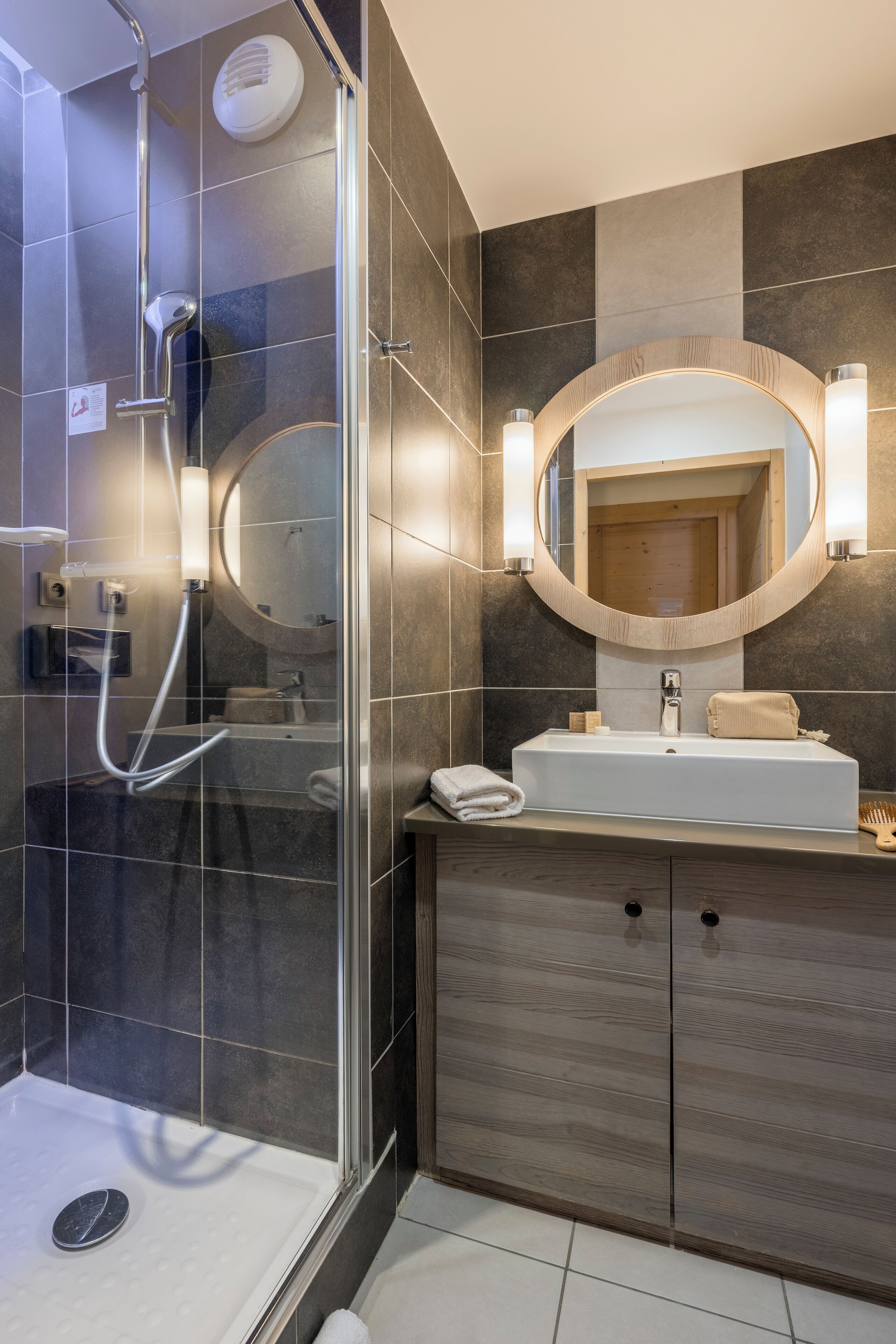 A modern bathroom with a glass-enclosed shower, a large mirror, and a wooden vanity.