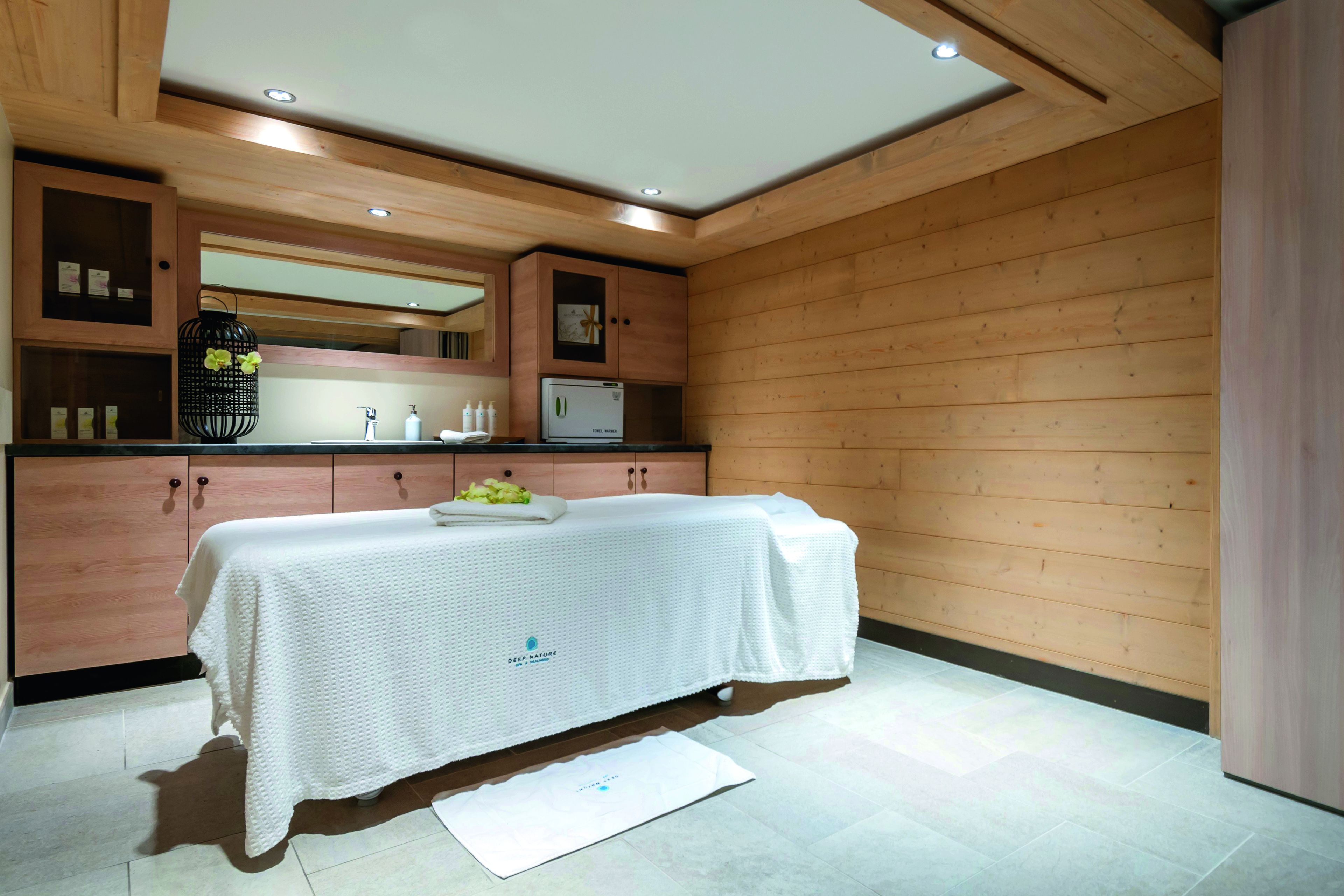 A modern spa room with wooden paneling, a massage table, a sink, and a mirror.
