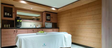 A modern spa room with wooden paneling, a massage table, a sink, and a mirror.