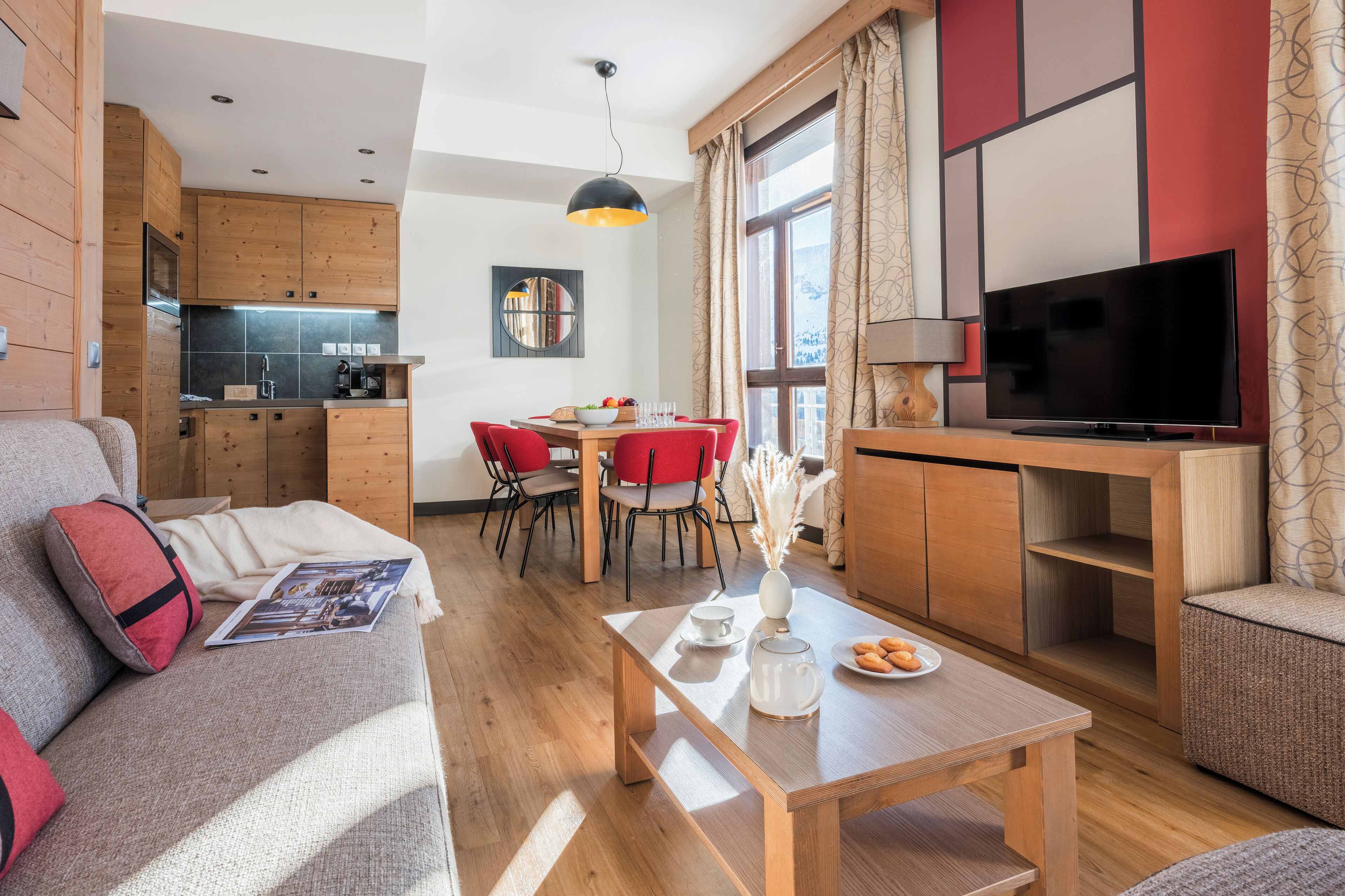 Una sala de estar moderna con un sofá, una mesa de centro, un televisor y un comedor con una mesa y sillas rojas.