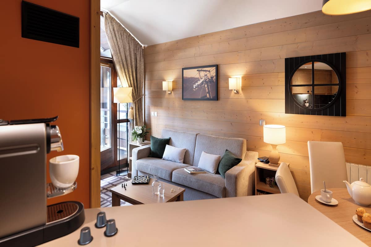 A hotel room with a wooden wall, a sofa, a coffee table, a tea set, and a window with curtains.