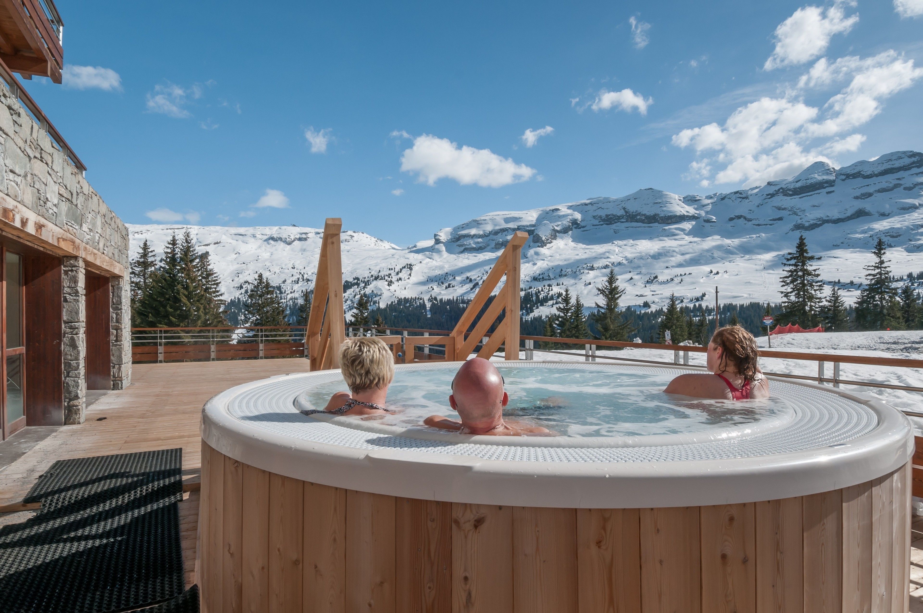 A wooden hot tub with a view of snow-covered mountains.