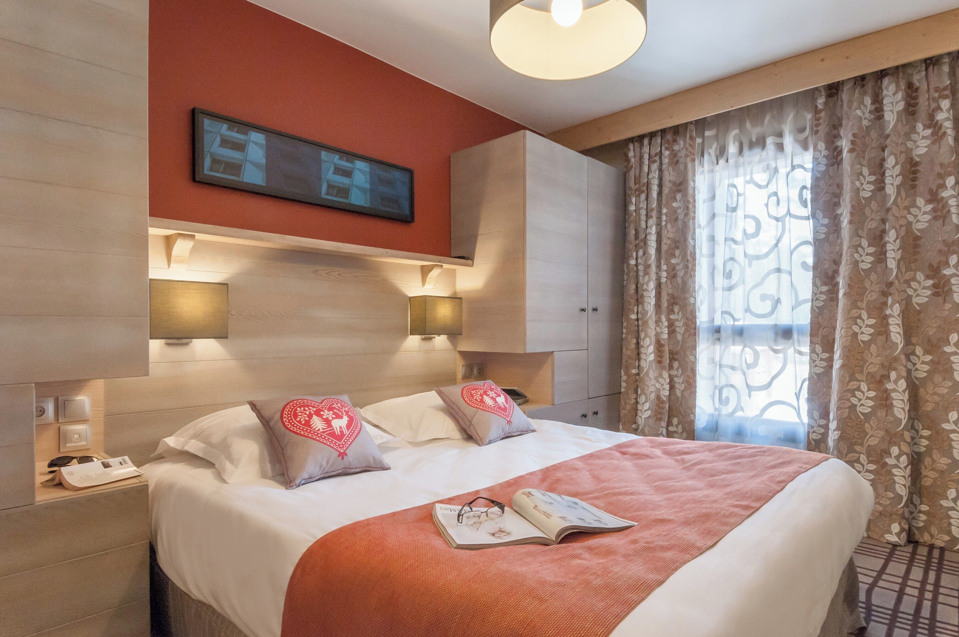 Ein Hotelzimmer mit einem Bett, zwei Nachttischlampen, einer Wanduhr und einem Fenster mit Vorhängen.
