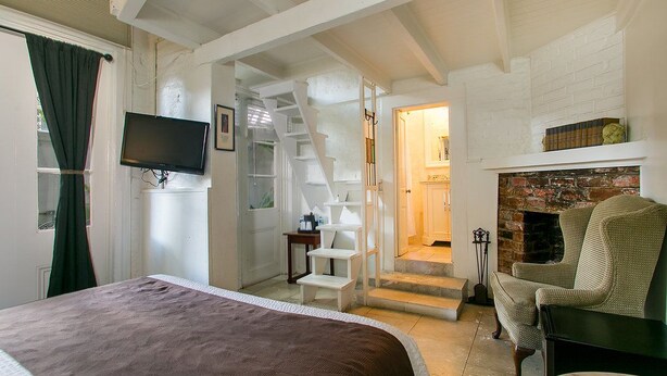 A bedroom with a bed, a television, a fireplace, and a staircase leading to another room. - Lafitte Hotel & Bar (New Orleans)