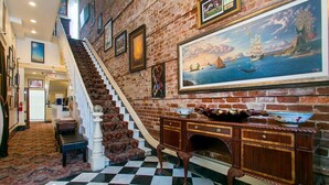 A grand staircase with a checkered floor leading to a landing with a large painting of a seascape. - Lafitte Hotel & Bar (New Orleans)