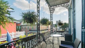 A balcony with wicker furniture, hanging plants, and a view of buildings. - Lafitte Hotel & Bar (New Orleans)