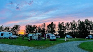 A campground with RVs parked on a gravel path, picnic tables, and a grassy field. - Airport Inn Motel & RV Park (Quesnel)