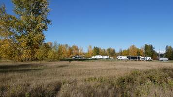 A field with several RVs parked, surrounded by trees with autumn foliage.