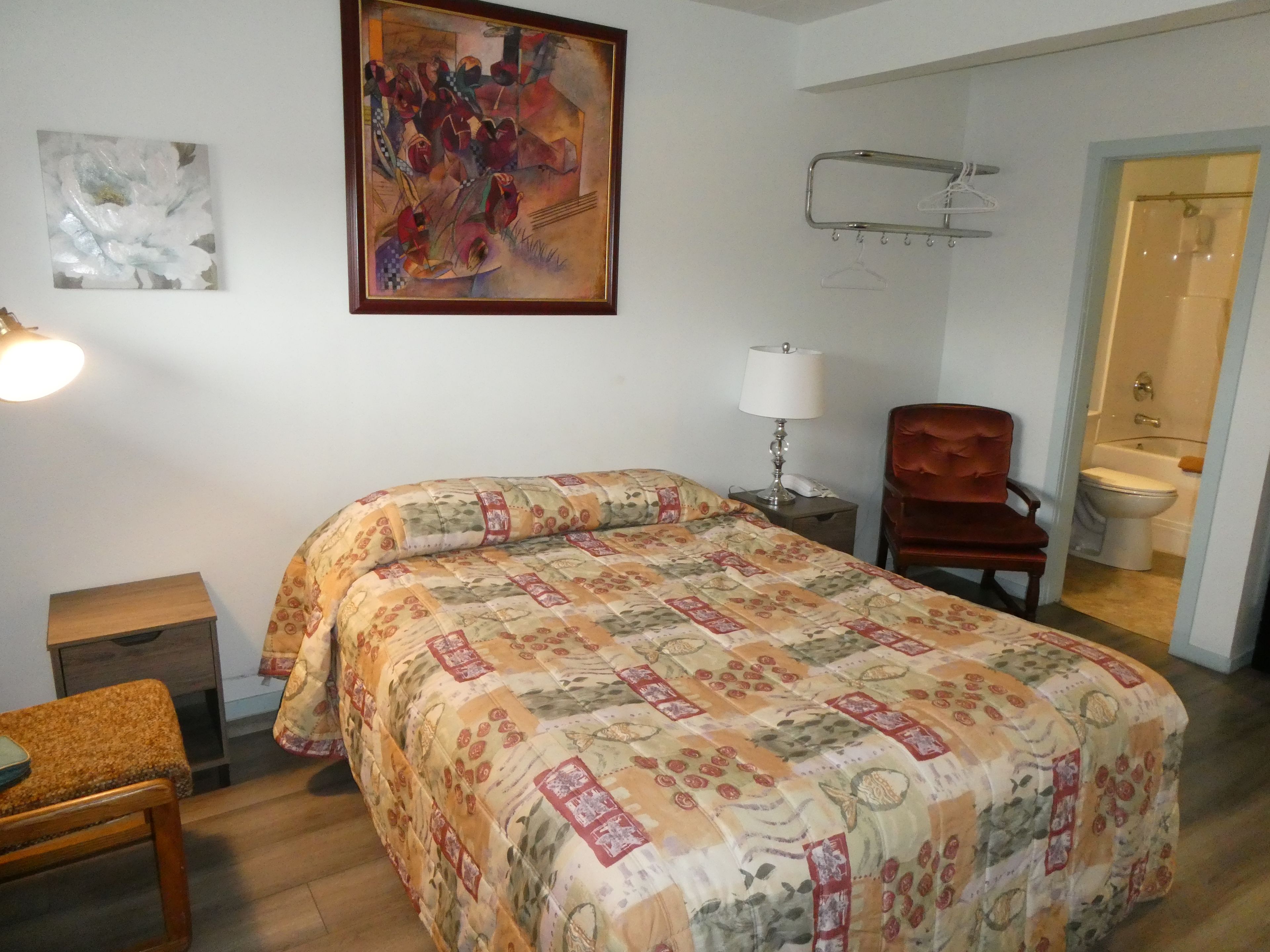 Ein Hotelzimmer mit Bett, Sessel, Nachttisch, Lampe, einem Bild an der Wand und einer Badezimmertür.