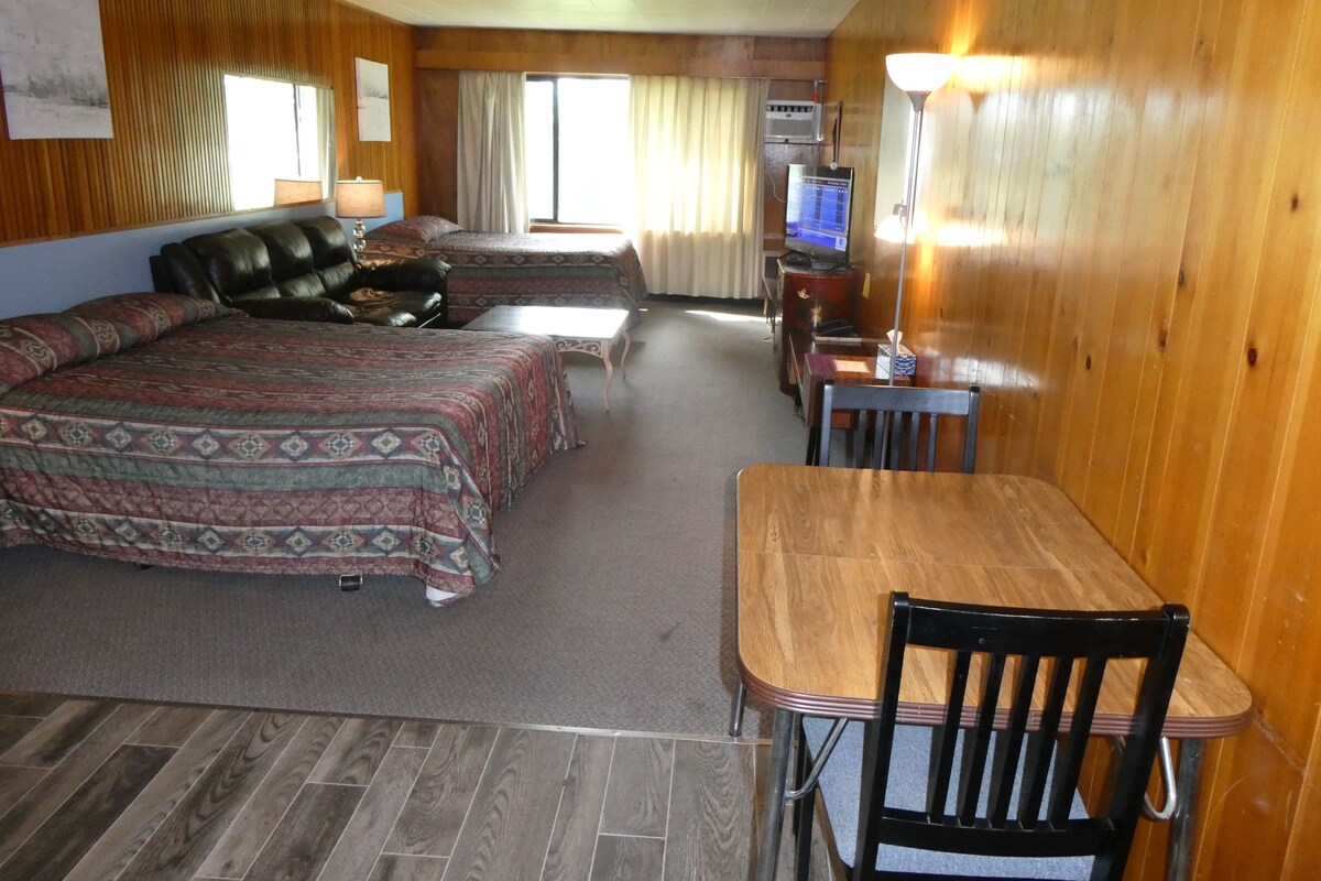 Een hotelkamer met een groot bed, een kleiner bed, een bureau, een stoel, een televisie en een raam met gordijnen.