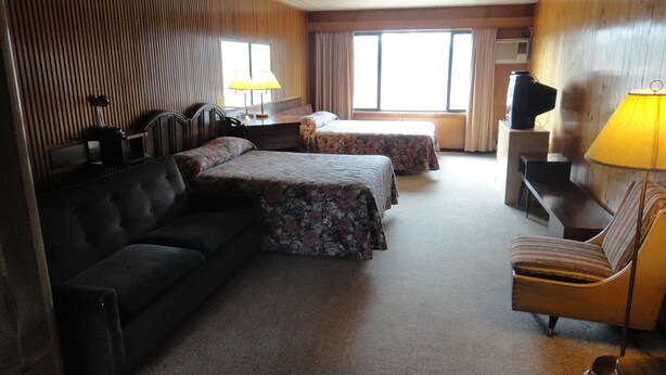 Una habitación de hotel con un sofá, dos camas con ropa de cama floral, un televisor y una lámpara.