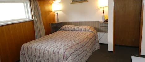 A hotel room with a bed, two bedside lamps, a painting on the wall, and a wooden wardrobe.