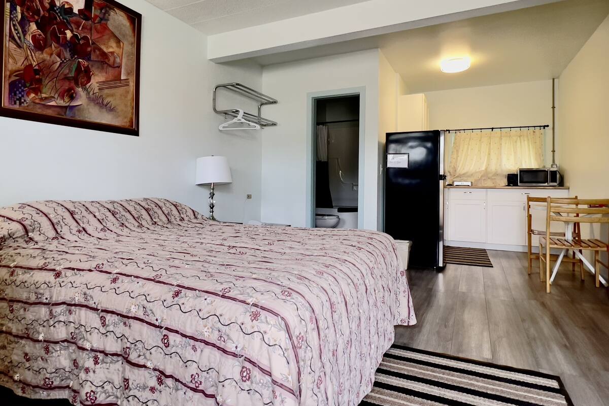 A bedroom with a bed, a desk, a refrigerator, and a microwave in the adjacent kitchenette.
