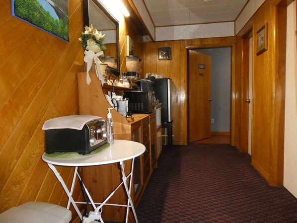 A hotel lobby with a wooden floor, a reception desk, a coffee machine, and a mirror. - Airport Inn Motel & RV Park (Quesnel)