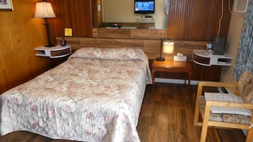 Een hotelkamer met een bed, een stoel, een bureau, een lamp, een televisie en een spiegel.