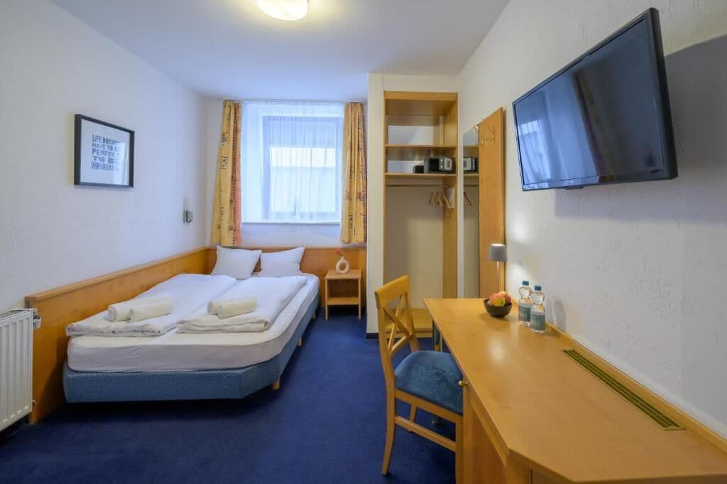 A hotel room with a bed, a desk, a chair, a television, and a window with curtains.