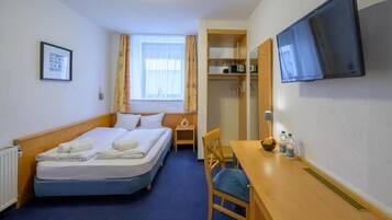 A hotel room with a bed, a desk, a chair, a television, and a window with curtains.