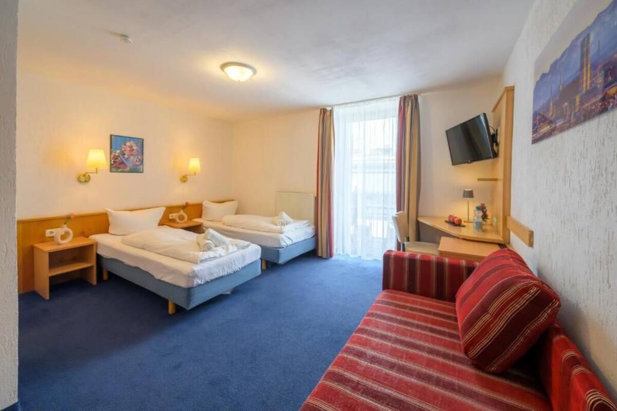 Habitación de hotel con dos camas, un sofá rojo, un televisor y una ventana con cortinas.