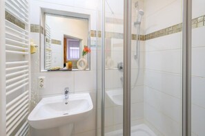 A bathroom with a white sink, a mirror, and a glass-enclosed shower. - Hotel Margit (Munich)
