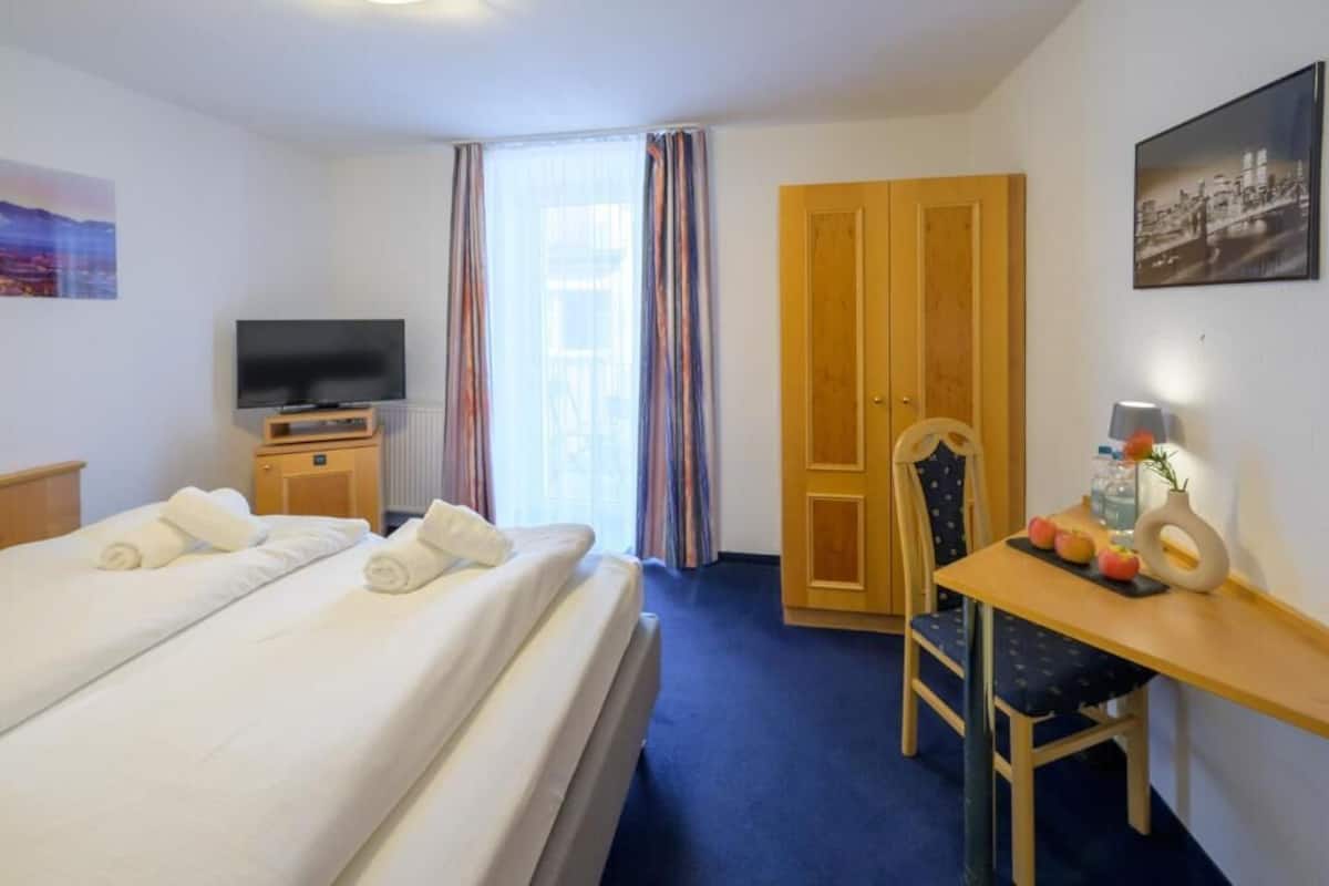 Una habitación de hotel con cama, televisión, escritorio y silla, y una puerta.
