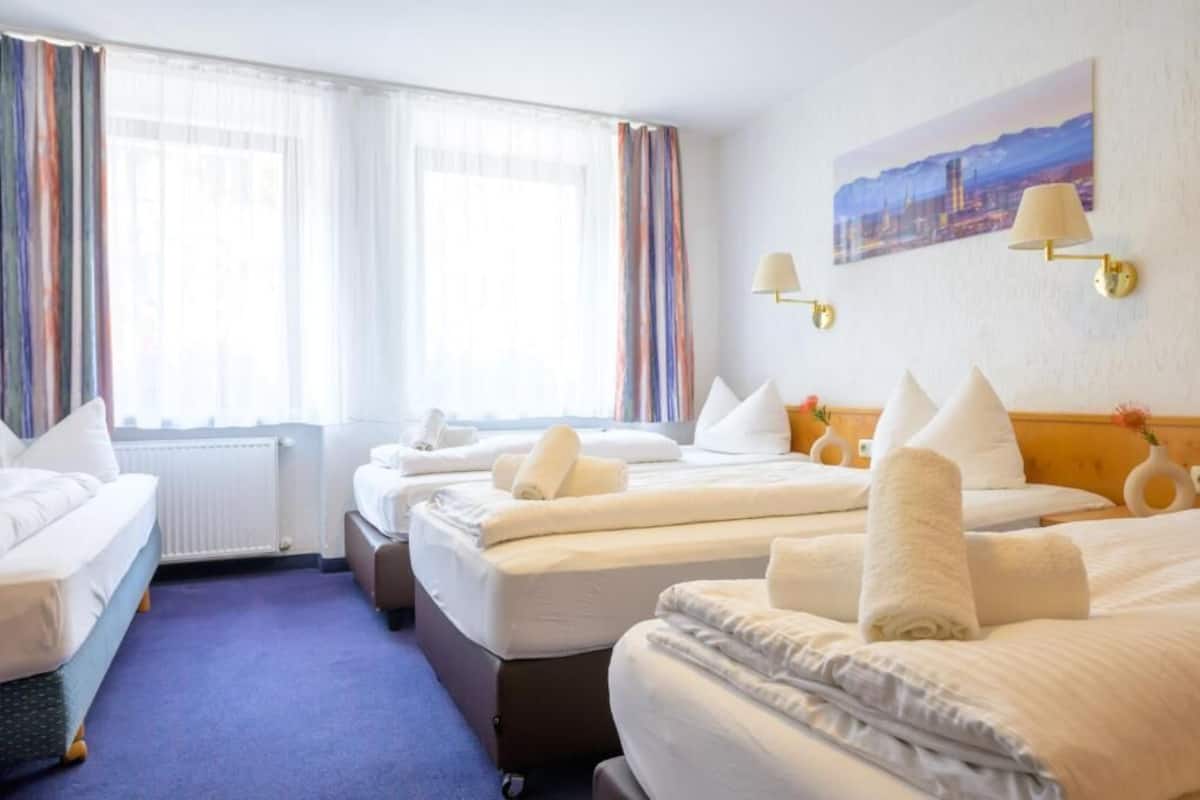 Habitación de hotel con dos camas, un sofá y un ventanal con cortinas.