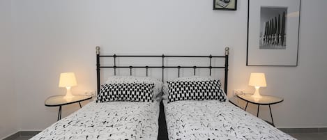 Un lit bien fait, recouvert d’une couvre-lit à motifs, deux tables de chevet avec des lampes et un tableau encadré au mur.
