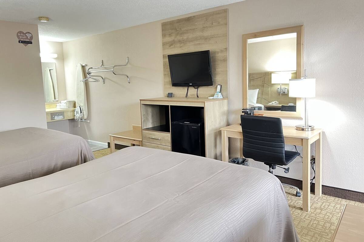 A hotel room with two beds, a desk with a chair, a television, a mirror, and a lamp.