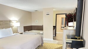 A hotel room with a large bed, a separate bathroom with a bathtub, a desk with a phone, and a mirror. - Viking Arms Inn (Ludington)