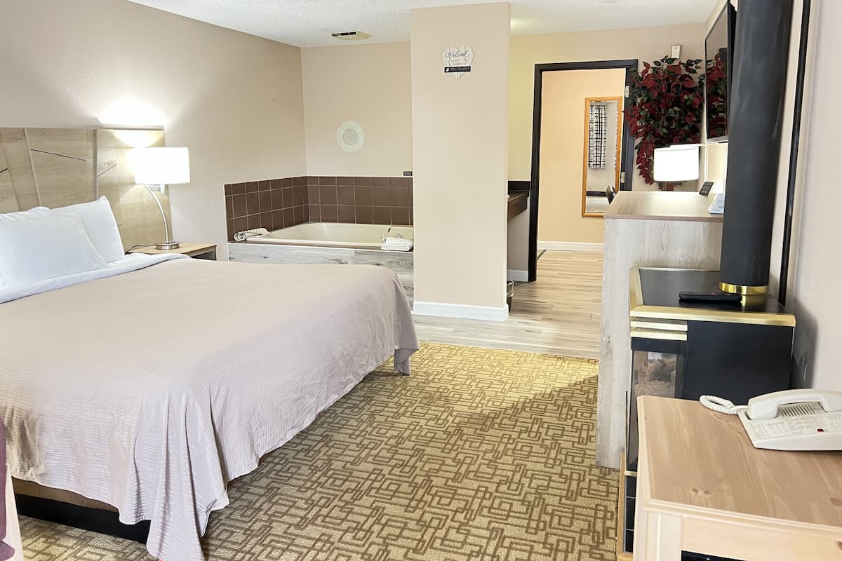 A hotel room with a large bed, a separate bathroom with a bathtub, a desk with a phone, and a mirror.