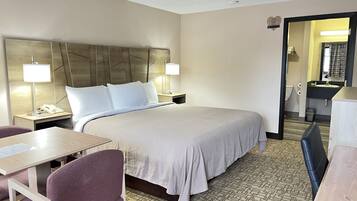 A hotel room with a large bed, bedside tables with lamps, a desk, a chair, and a bathroom visible through an open door.