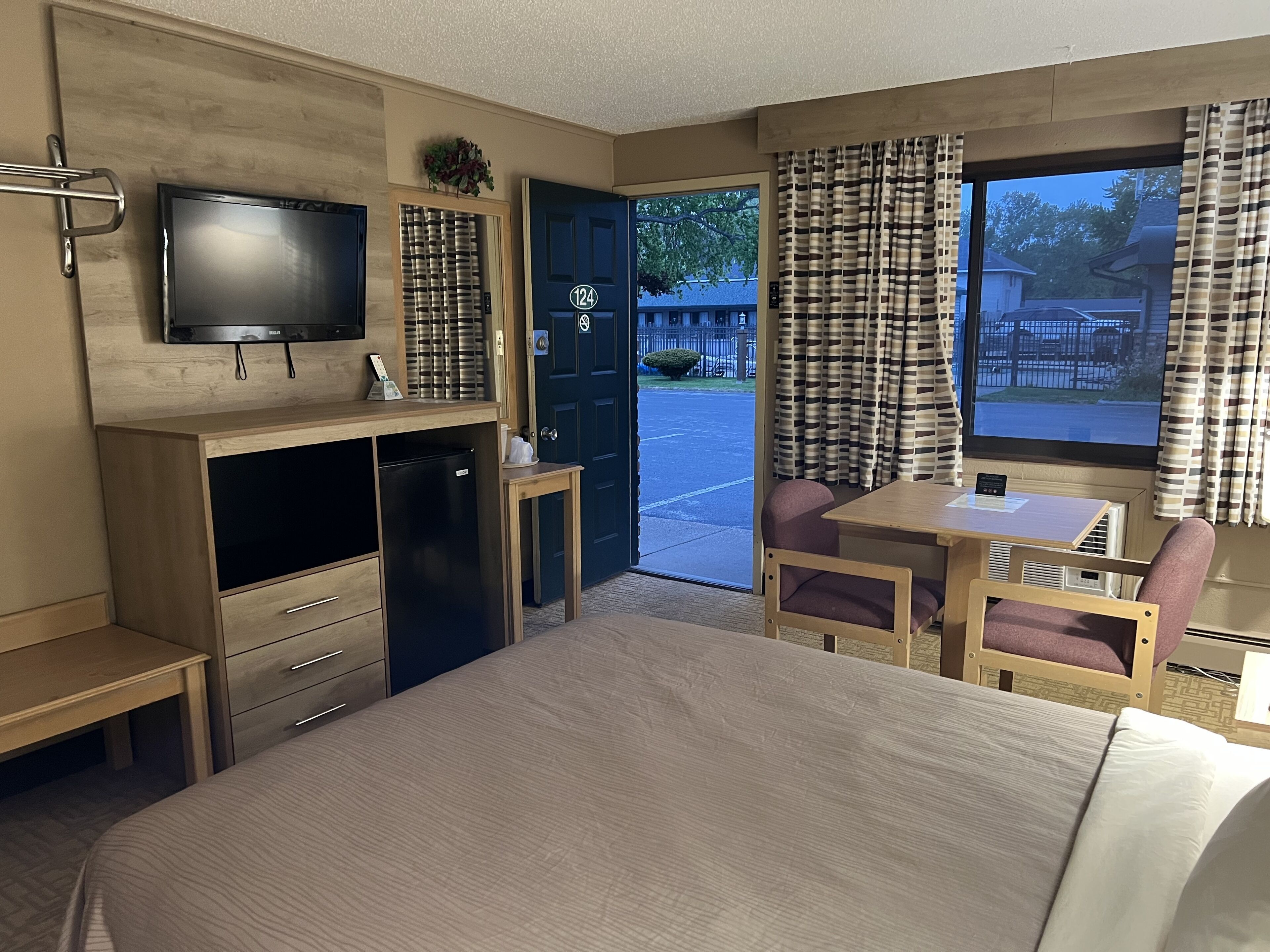 A hotel room with a bed, a desk, a chair, a television, and a window with curtains.