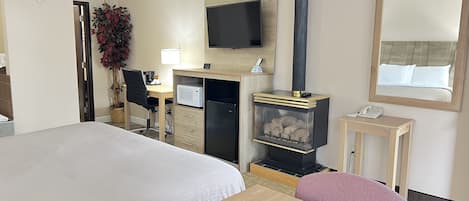 A hotel room with a bed, a desk, a television, a fireplace, and a mirror.